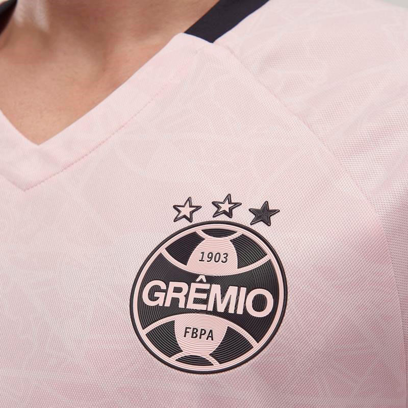 Close no escudo do Grêmio na camisa masculina Outubro Rosa 2025, detalhamento do tecido e logo Umbro